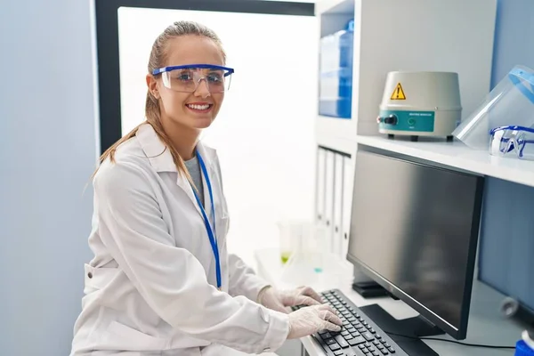 研究室で働くコンピュータを使って科学者の制服を着た若いブロンドの女性 — ストック写真