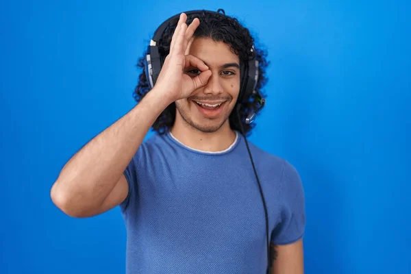 头发卷曲的西班牙裔男人 一边用耳机听音乐 一边做着手势 一边微笑着 眼睛看着手指 面带笑容 — 图库照片