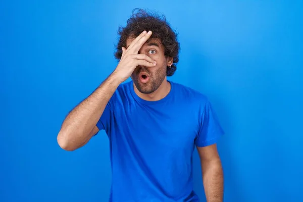 Hispanic Young Man Standing Blue Background Peeking Shock Covering Face — Foto Stock