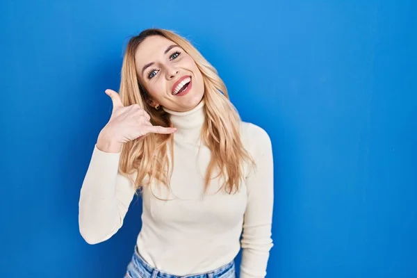 青い背景の上に立つ若い白人女性は 電話で話すような手と指で電話のジェスチャーをして笑っています コミュニケーションの概念 — ストック写真