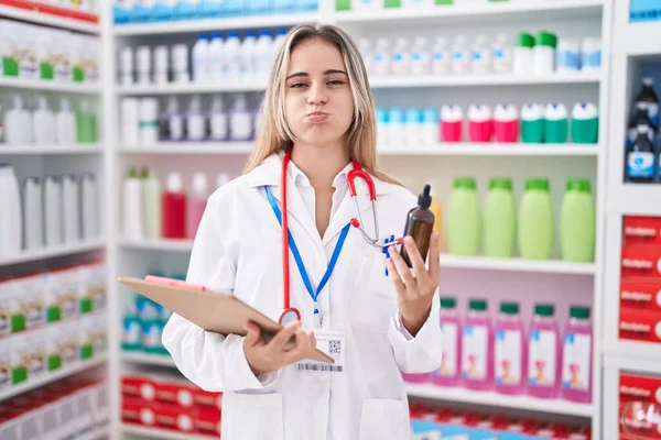 Молодая Блондинка Работающая Аптеке Держит Бутылочку Пыхтящими Щеками Смешным Лицом — стоковое фото