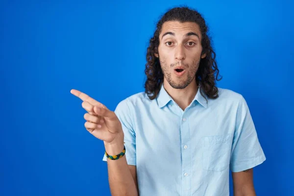 Young Hispanic Man Standing Blue Background Surprised Pointing Finger Side — Fotografia de Stock