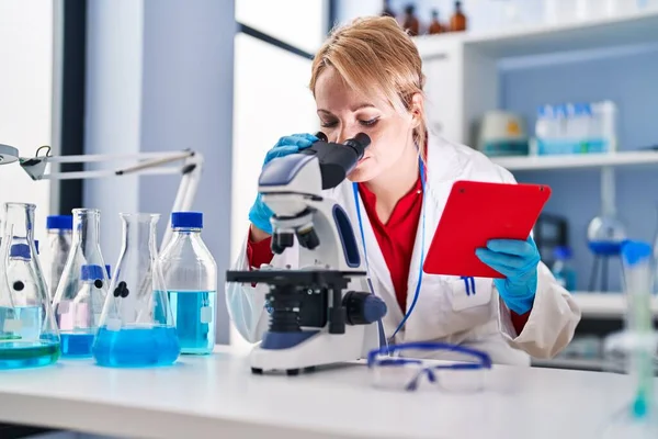 年轻的金发女科学家在实验室使用触摸板和显微镜 — 图库照片