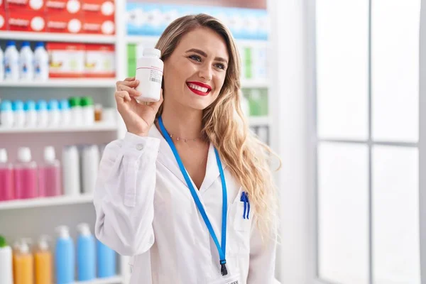Jovem Bela Mulher Hispânica Farmacêutico Sorrindo Confiante Segurando Pílulas Garrafa — Fotografia de Stock