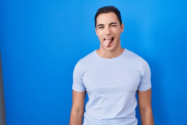 Homem Hispânico Jovem Sobre Fundo Azul Furando Língua Para Fora — Fotografia de Stock