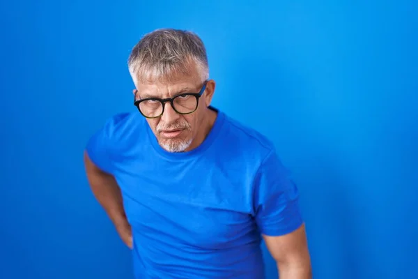 头发灰白的西班牙裔男子站在蓝色的背脊上 用手触摸 肌肉疼痛 — 图库照片