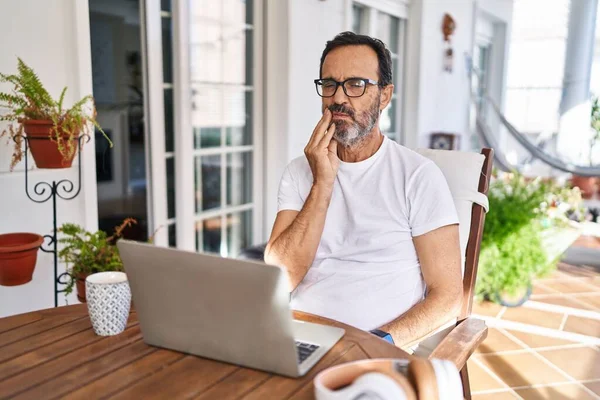 Middle age man using computer laptop at home touching mouth with hand with painful expression because of toothache or dental illness on teeth. dentist