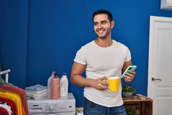 Genç Spanyol Adam Akıllı Telefon Kullanıyor Kahve Içiyor Çamaşır Odasında — Stok fotoğraf
