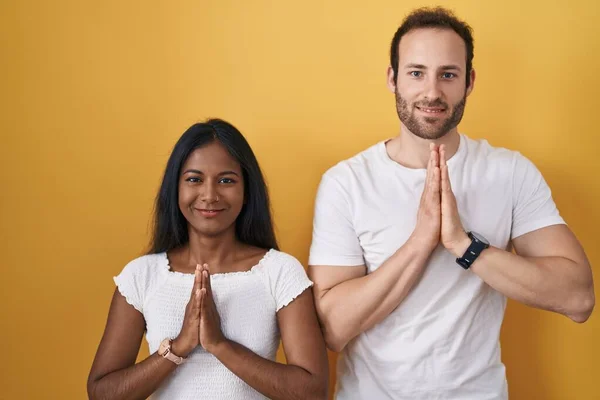 Interracial Couple Standing Yellow Background Praying Hands Together Asking Forgiveness — Stock Photo, Image