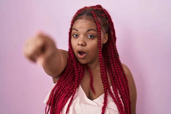 非洲裔美国女人 辫子式的头发 站在粉色的背景上 指尖着前方的手指 惊讶的张开的嘴 惊讶的表情 前面有什么东西 — 图库照片