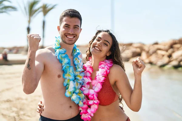 若いヒスパニック系のカップルは誇りに思って叫んでビーチでハワイのネックレスを身に着けています 勝利と成功を祝う非常に腕を上げ興奮して — ストック写真