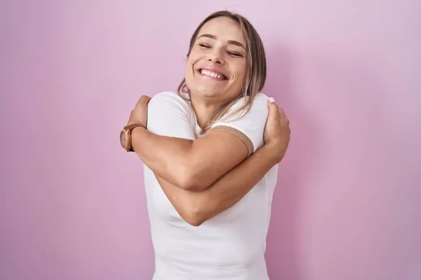 Blonde Caucasian Woman Standing Pink Background Hugging Oneself Happy Positive — Stok fotoğraf