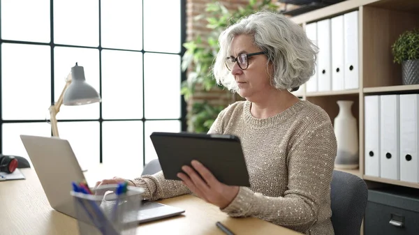 在办公室使用触摸板和笔记本电脑的中年妇女与灰发商人 — 图库照片