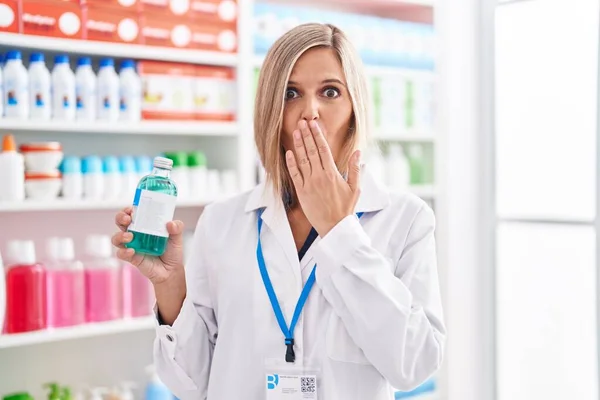 薬局で働いているブロンドの女性は 手で口を覆い ショックを受け 間違いを恐れてシロップを持っています 驚きの表情 — ストック写真