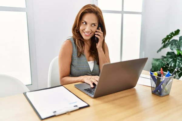 年轻的拉丁女商人使用笔记本电脑 在办公室用智能手机交谈 — 图库照片