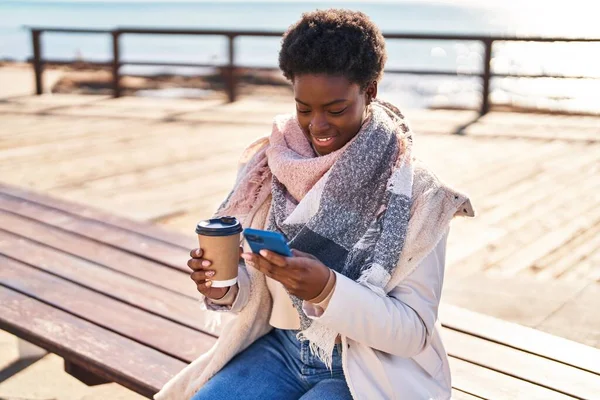 Mujer Afroamericana Usando Teléfono Inteligente Bebiendo Café Sentado Banco Playa — Foto de Stock