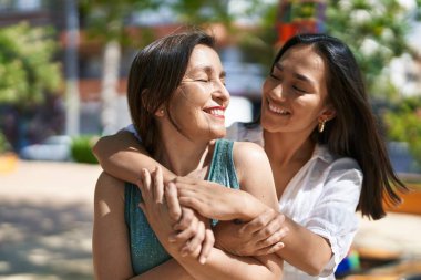 Two women mother and daughter smiling confident hugging each other at park