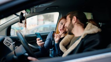 Man and woman couple using smartphone driving car at street