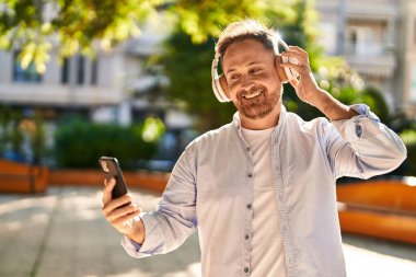 Parkta müzik dinlerken kendinden emin gülümseyen beyaz bir genç.