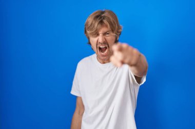 Middle age man standing over blue background pointing displeased and frustrated to the camera, angry and furious with you 