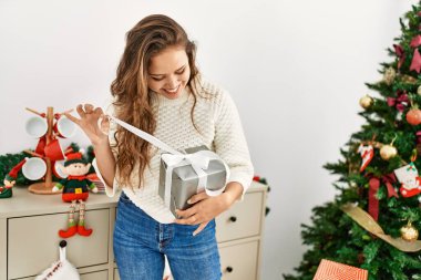 Genç, güzel, İspanyol bir kadın gülümseyerek evinde kendine güvenen bir Noel hediyesi açıyor.