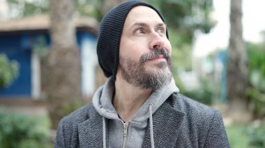 Genç kel adam parkın kenarına bakarak gülümsüyor.