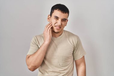 Günlük tişört giyen genç bir Arap diş ağrısı ya da diş hastalığından dolayı acı dolu bir ifadeyle ağıza dokunuyor. dişçi 