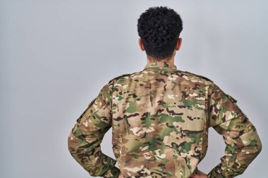 Kamuflaj üniforması giyen bir Arap geriye doğru bakıyor ve kollarını vücuduna dikiyor. 