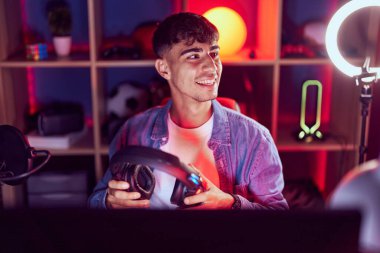 Oyun odasında kulaklık tutarak gülümseyen İspanyol asıllı genç adam.