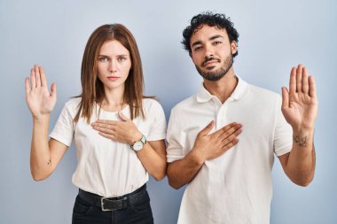 Gündelik giysiler içinde el ele tutuşup el pençe divan durarak sadakat yemini eden genç bir çift. 