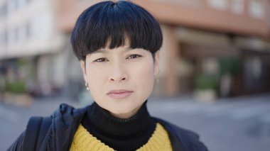 Young chinese woman standing with serious expression at street