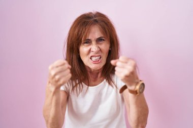 Orta yaşlı bir kadın öfkeyle bağırırken kızgın ve kızgın yumruklarını kaldırıyor. öfke ve agresif konsept. 