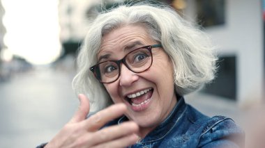 Middle age woman with grey hair smiling confident having video call at street