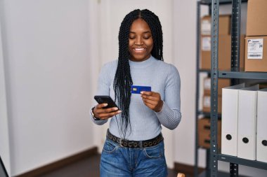 Afrika kökenli Amerikalı kadın ekommerans işçisi. Ofiste akıllı telefon ve kredi kartı kullanıyor.