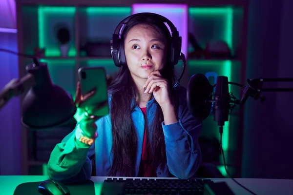 Mladá Asiatka Hrající Videohry Chytrým Telefonem Rukou Bradě Přemýšlející Otázce — Stock fotografie