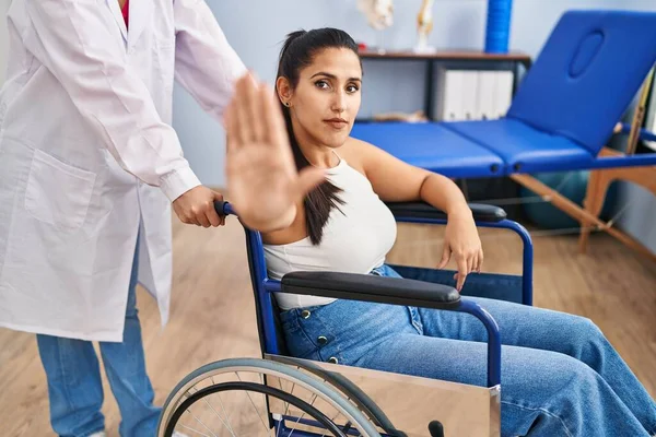 年轻的惊慌失措的女人坐在理疗诊所的轮椅上 张开手 严肃而自信地做着止步手势 做着防守动作 — 图库照片