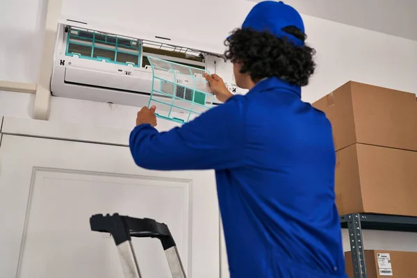 若いヒスパニック系の男性技術者がオフィスでエアコンを修理する — ストック写真