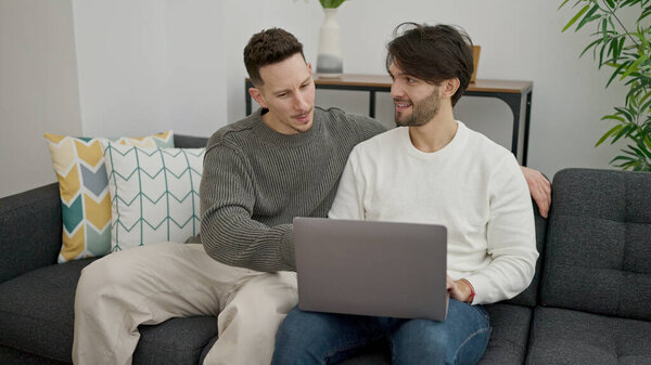Двое мужчин сидят дома на диване с ноутбуком