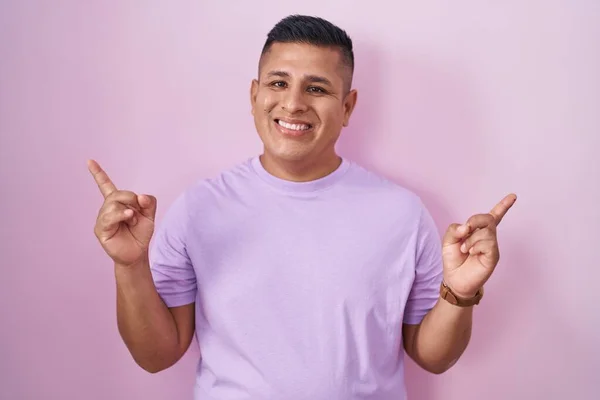 年轻的惊慌失措的男人站在粉红的背景上 带着自信的微笑 用手指指向不同的方向 复制广告空间 — 图库照片