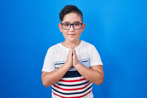 Νεαρό Ισπανόφωνο Παιδί Στέκεται Πάνω Από Μπλε Φόντο Προσεύχεται Χέρια — Φωτογραφία Αρχείου