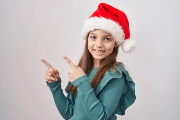 小さなCaucasian女の子身に着けているクリスマスの帽子笑顔と見てカメラを指しています二つの手と指で側面 — ストック写真