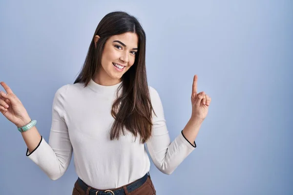 若いブルネットの女性は 異なる方向への指で自信を持って指して笑みを浮かべて青色の背景に立っている 広告のコピースペース — ストック写真