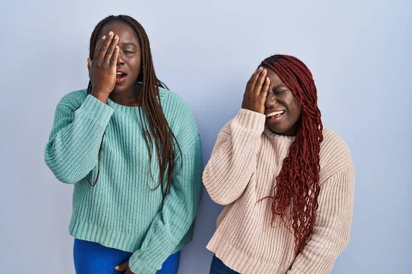青い背景の上に立っている2人のアフリカ人女性は 半分の顔 口を手で覆い疲れて叫んでいます 痛みで顔が痛い — ストック写真