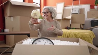 Middle age woman with grey hair unpacking cardboard box at new home