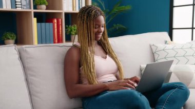 African american woman using laptop sitting on sofa at home