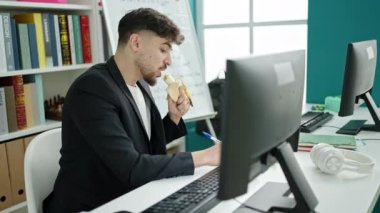 Genç Arap öğrenci üniversite sınıfında bilgisayar kullanarak muz yiyor.