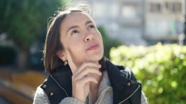 Young beautiful hispanic woman standing with doubt expression at park
