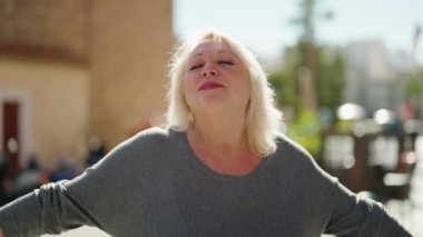 Middle age blonde woman smiling confident breathing at street