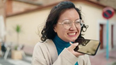 Genç Çinli kadın gülümsüyor caddede akıllı telefondan konuşuyor.