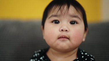 Adorable hispanic baby sitting on sofa with relaxed expression at home